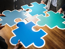 Hands holding four large puzzle pieces over a desk